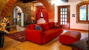 Un sofá rojo en una habitación con arcos de piedra, una puerta de madera y vistas a través de una ventana.