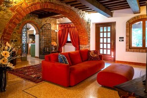 Ein rotes Sofa in einem Raum mit Steinbögen, einer Holztür und einem Ausblick durch ein Fenster.