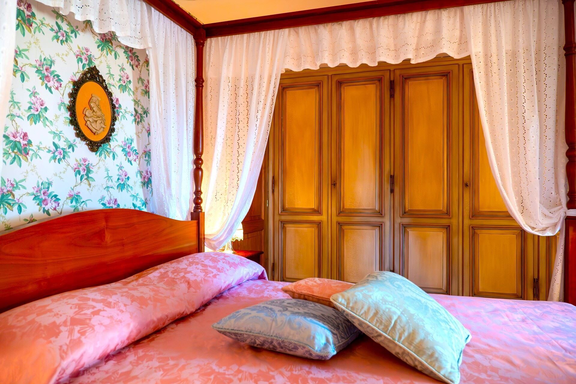 Une chambre à coucher avec un lit en bois, un papier peint à motifs floraux et une grande armoire.