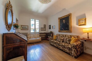 Ein Zimmer mit Holzboden, einer Couch, einem Schreibtisch, einem großen gerahmten Porträt und einem Fenster.