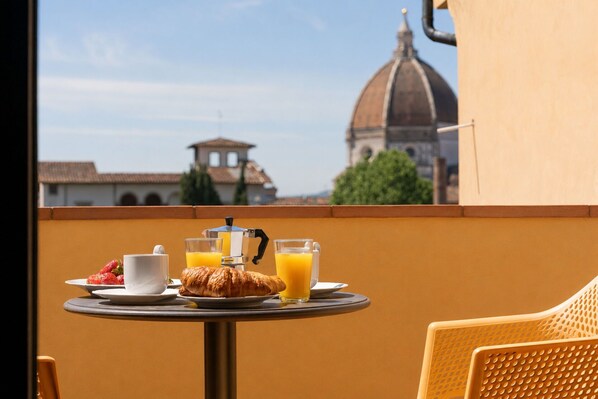 Ein Tisch mit Frühstücksangeboten, darunter Croissants, Kaffee und Orangensaft, mit Blick auf ein historisches Gebäude im Hintergrund.
