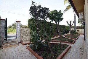 Ein gepflasterter Außenbereich mit einer Steinmauer, einem Metallgitter und einer Reihe von Pflanzkästen mit verschiedenen Pflanzen.