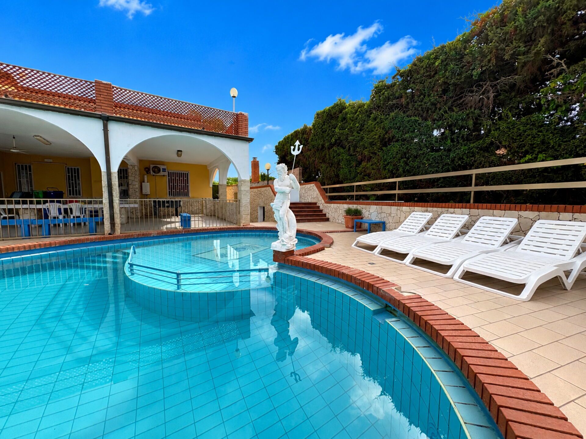 A swimming pool with a statue, lounge chairs, and a covered patio area.