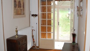 Een kamer met houten vloer, een houten dressoir, een lamp, een deur met ruitpanelen en een lijst met een afbeelding aan de muur.