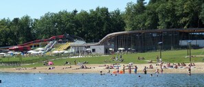 Ein Seehotel mit Badesteg, Wasserrutsche und überdachter Schutzhütte.