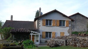 Een tweelaags huis met een pannendak, houten luiken en stenen muren.