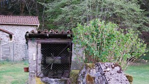 Een rustieke stenen constructie met een metalen hek, omringd door groen en een stenen gebouw op de achtergrond.
