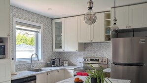 Une cuisine moderne avec des armoires blanches, un comptoir en marbre, un réfrigérateur en acier inoxydable et un luminaire suspendu.
