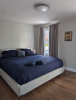 A bedroom with a bed, pillows, a folded blanket, a window with curtains, and a framed picture on the wall.