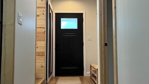 Um corredor com piso de madeira, uma porta preta com janela e um acessório de iluminação no teto.