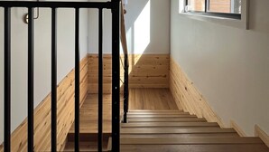 Uma escadaria de madeira com corrimão preto, que leva a um quarto com uma janela grande e parede branca.