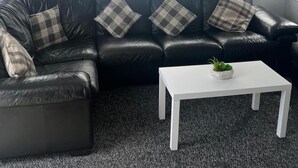 A black leather sofa with plaid cushions, a white coffee table with a plant, and a grey carpet. - Skegness 2-bed Caravan, Sleeps 6, 6 Mins to Beach (Skegness)
