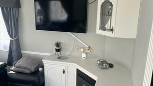 A room with a flat-screen TV mounted on the wall, a small potted plant, a cabinet with a mirror, and a toy car on the counter. - Skegness 2-bed Caravan, Sleeps 6, 6 Mins to Beach (Skegness)