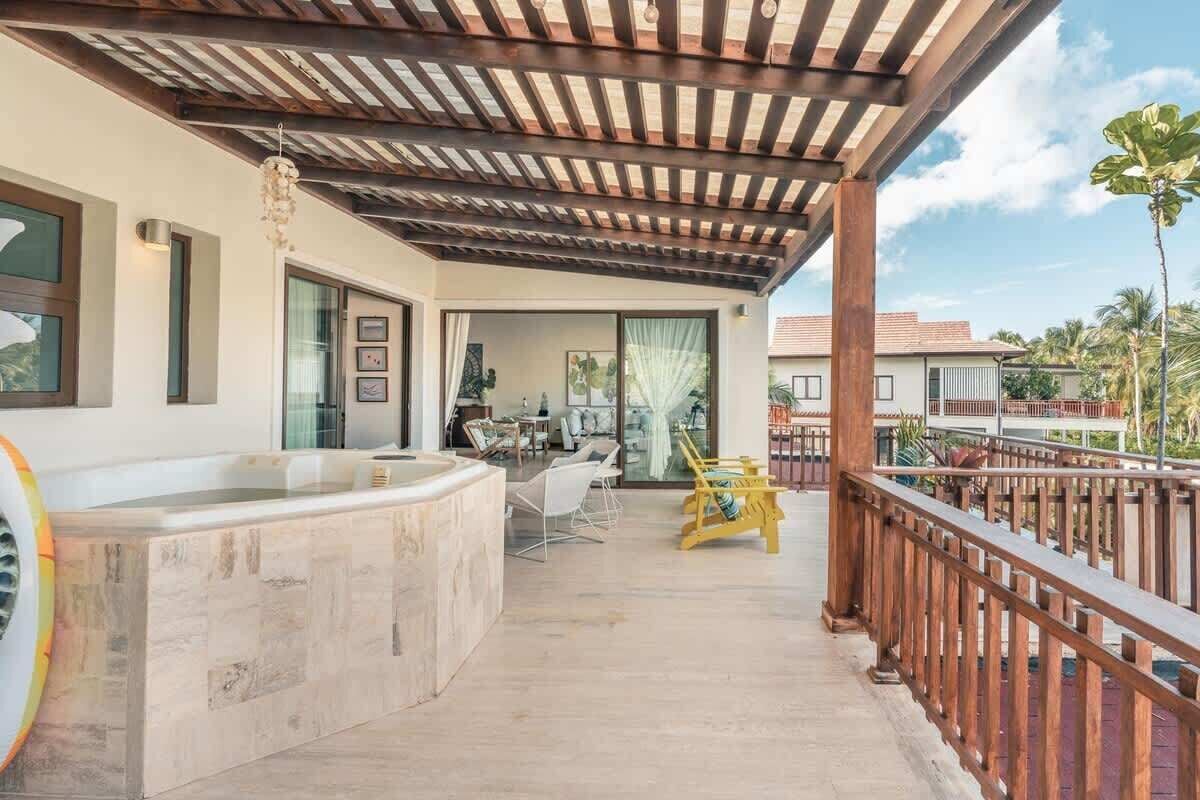 A covered outdoor area with a hot tub, wooden deck, and a view of a residential building.