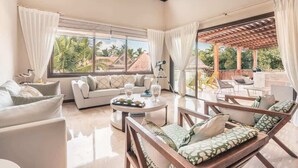 Ein geräumiges Wohnzimmer mit einer Couch, Sesseln, einem Couchtisch und Blick ins Freie.
