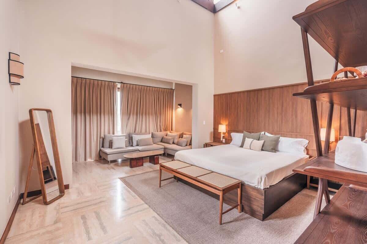 Ein modernes Hotelzimmer mit einem großen Bett, einer Couch, einem Holfnitztisch und einem Spiegel.
