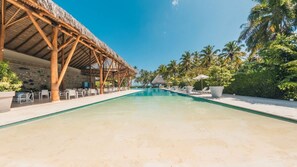 A pool area with a thatched-roof structure, lounge chairs, and palm trees. - Apex Executive Apartments - Port (Las Terrenas)