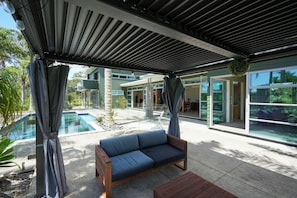 A covered outdoor area with a pool, a wooden bench, and a sofa.