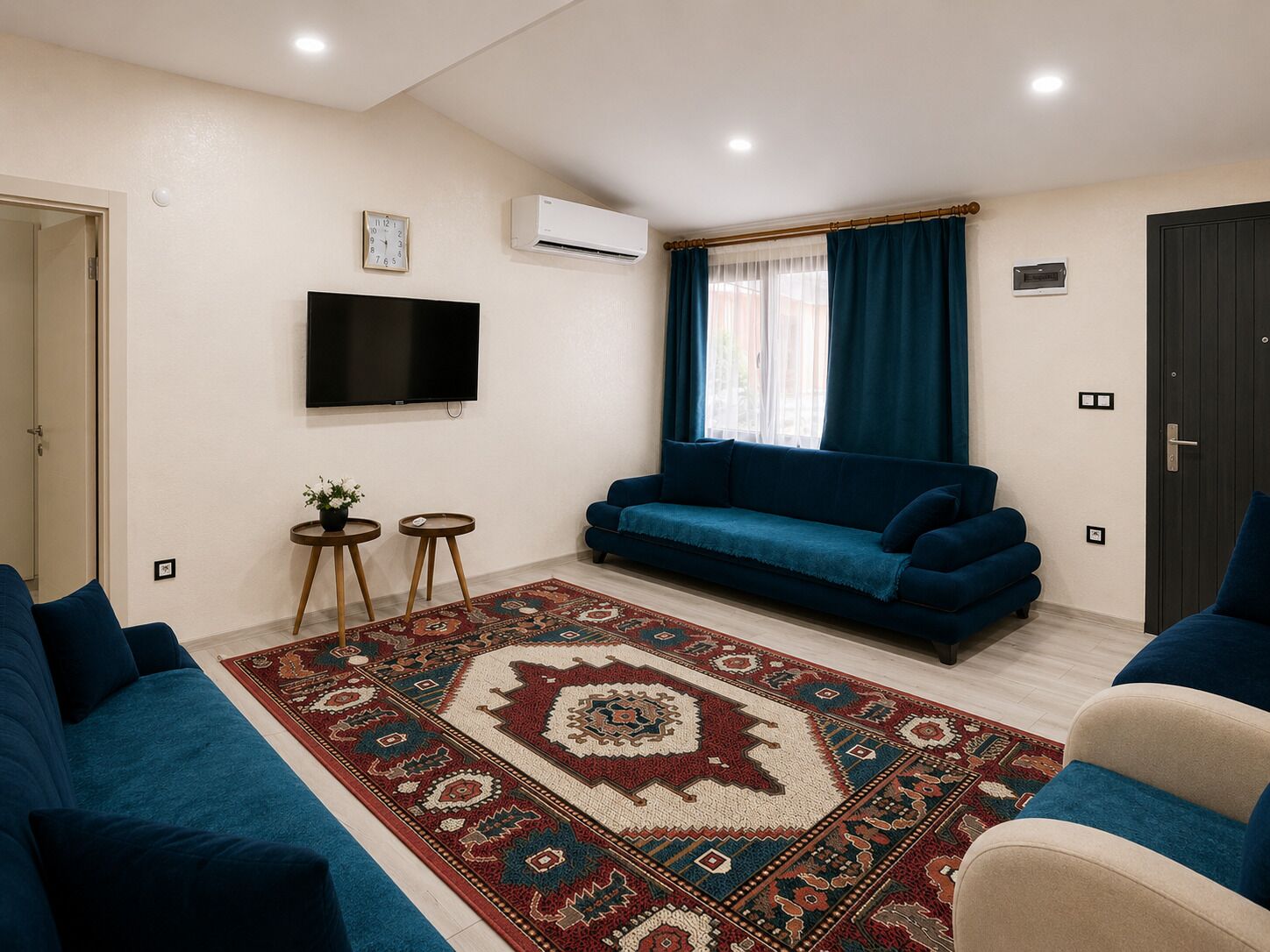 A living room with a blue sofa, a patterned rug, a flat-screen TV, and a window with curtains.