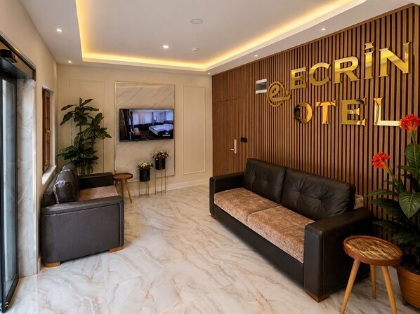 A hotel lobby with a sofa, a television, and a reception desk. - ECRİN OTEL (Çaykara)