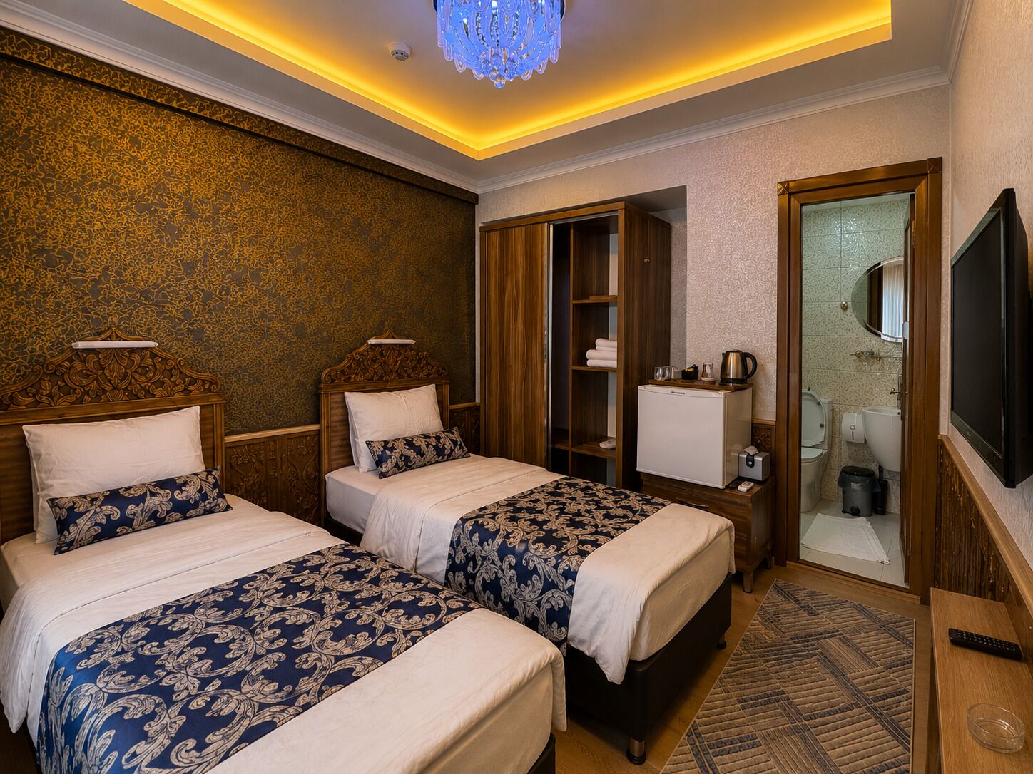 A hotel room with two beds, a minibar, a television, and a bathroom visible through an open door.