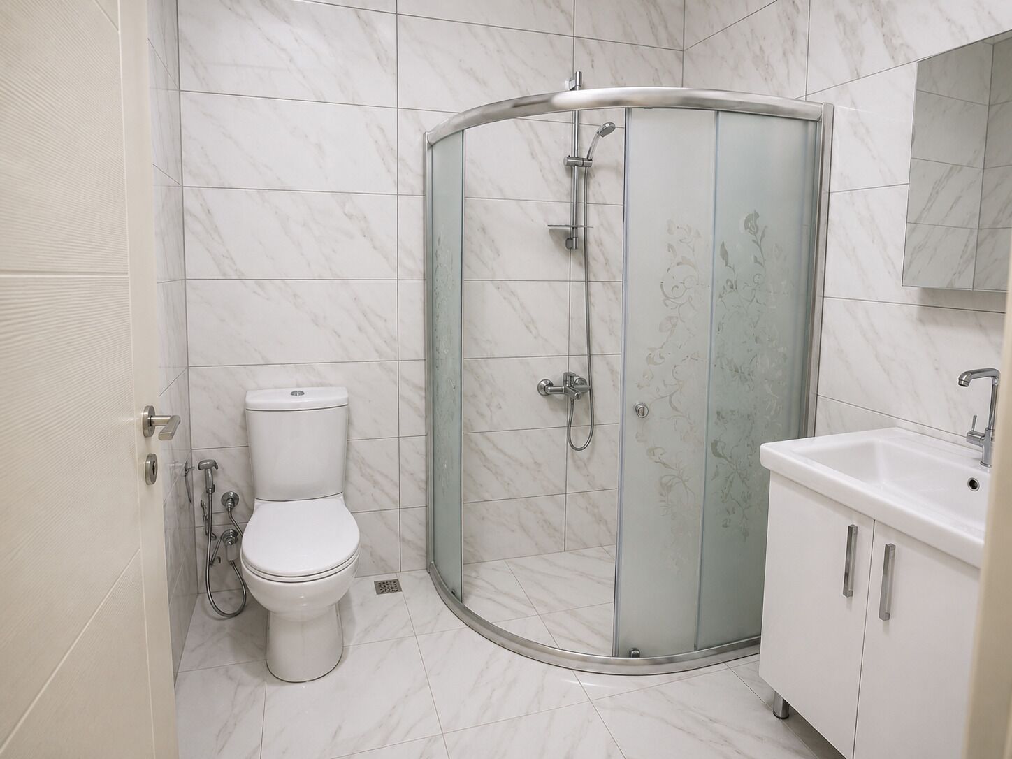 A bathroom with a glass-enclosed shower, a toilet, and a sink with a cabinet.