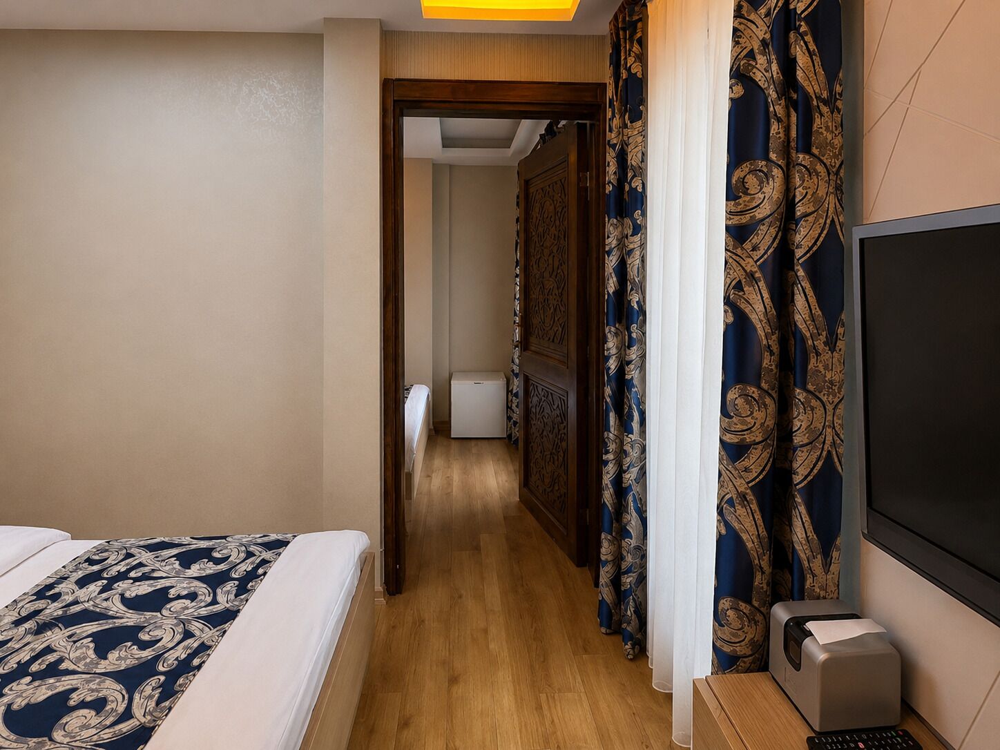 A hotel room with a bed, a desk with a printer, and a TV.