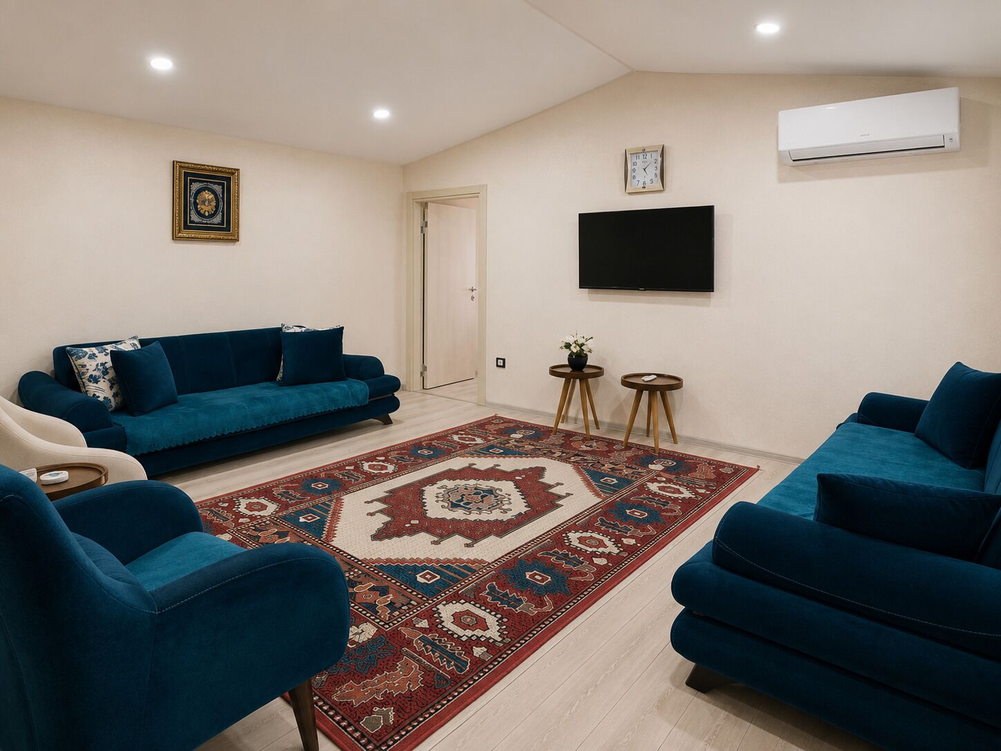 A living room with a blue sofa set, a patterned rug, a flat-screen TV, and an air conditioning unit.
