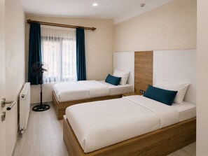 Una camera d'albergo con due letti, una ventola e una finestra con tende.