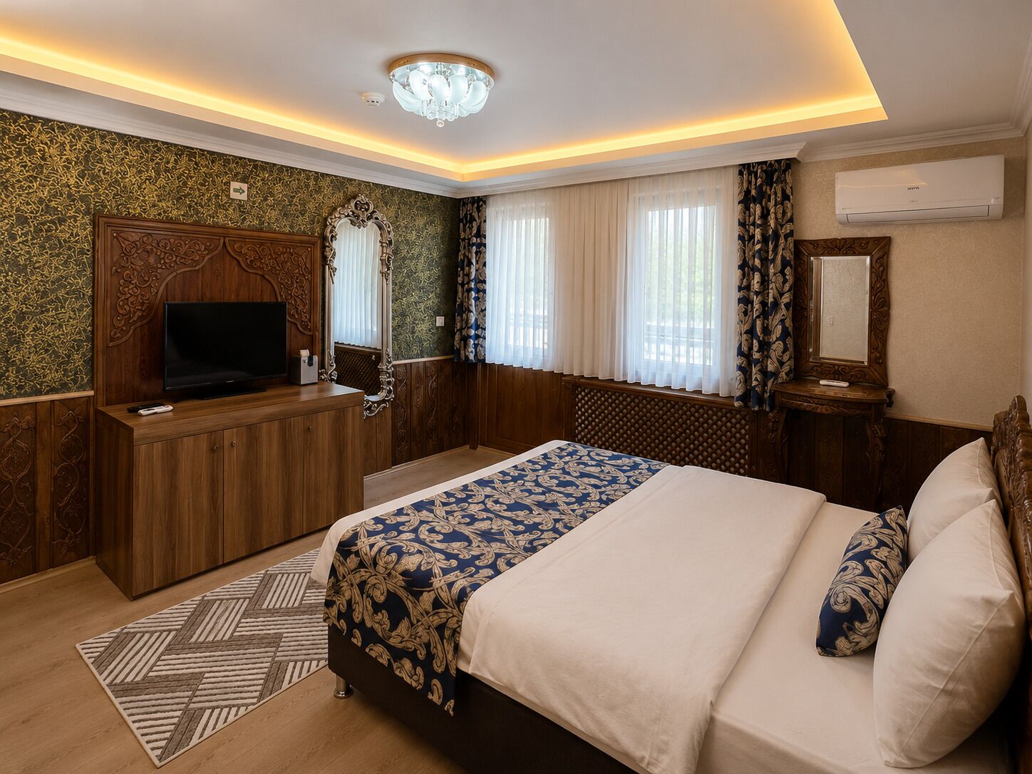 A hotel room with a bed, a TV, a mirror, and a window with curtains.