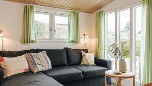 A modern living room with a sectional sofa, a small round table, and a potted plant. - 6 Person Holiday Home in Vaeggerlose (Vaeggerlose)