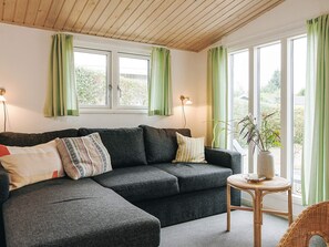 A modern living room with a sectional sofa, a small round table, and a potted plant. - 6 Person Holiday Home in Vaeggerlose (Vaeggerlose)