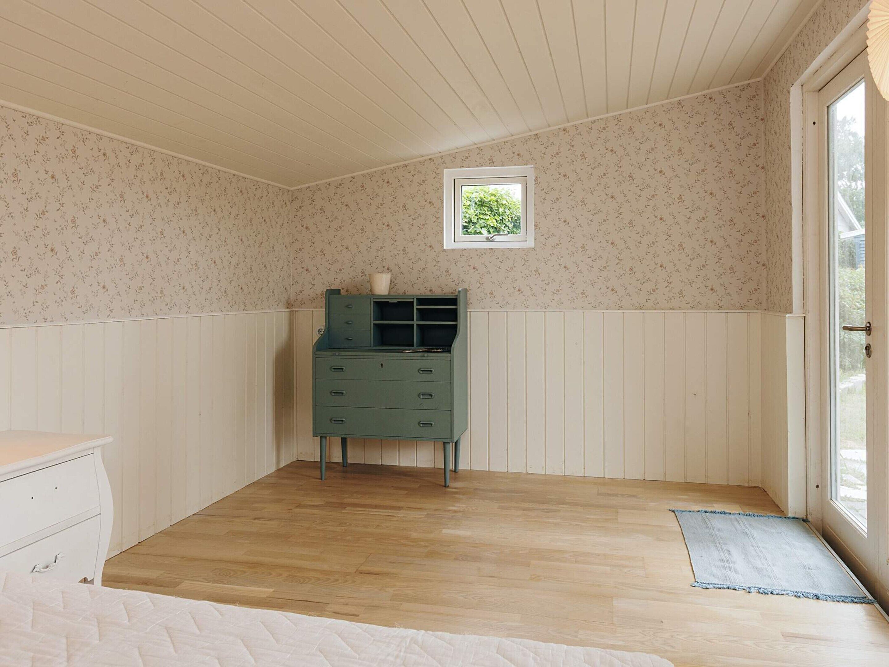 Een kamer met een houten vloer, een groene kast, een klein raam en een deur naar buiten.