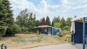 A blue house with a covered porch, surrounded by a garden and trees. - 6 Person Holiday Home in Vaeggerlose (Vaeggerlose)