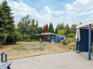 A blue house with a covered porch, surrounded by a garden and trees. - 6 Person Holiday Home in Vaeggerlose (Vaeggerlose)