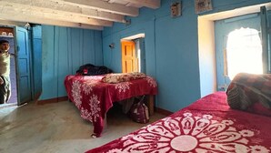 Una habitación con una cama, una mesa con mantel rojo, pared azul y techo de madera.