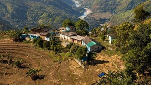 Un paisaje montañoso con campos en terrazas y un pequeño asentamiento con casas tradicionales.