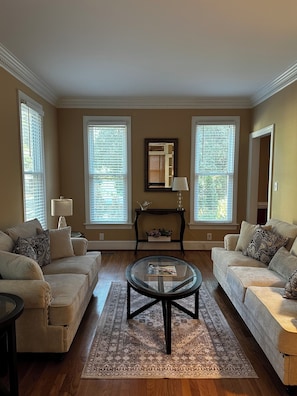 A living room with two beige sofas, a glass coffee table, a dark console table with a lamp, and a large mirror on the wall. - Cozy luxe Durham escape (Durham)