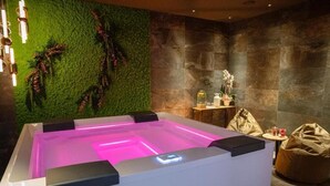 A spa area with a heated pool, a green wall with plants, a stone wall, and a small table with a statue.