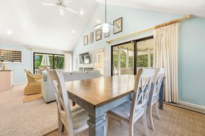 A dining area with a wooden table, chairs, a television, and a view of the outdoors. - Sandy Paws: Dog-friendly, Corolla Light Amenities (Corolla)