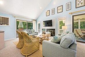 A living room with a fireplace, wicker chairs, a sofa, and a television. - Sandy Paws: Dog-friendly, Corolla Light Amenities (Corolla)