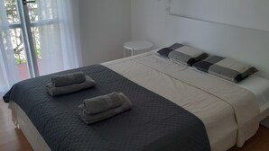 A neatly made bed with a quilted headboard, a small round table beside it, and a window with sheer curtains. - One bedroom apartment with balcony and garden view (Selce)