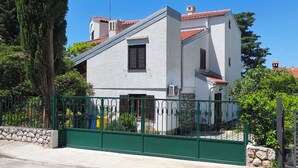 A two-story building with a white facade, red-tiled roof, and a green metal gate. - One bedroom apartment with balcony and garden view (Selce)