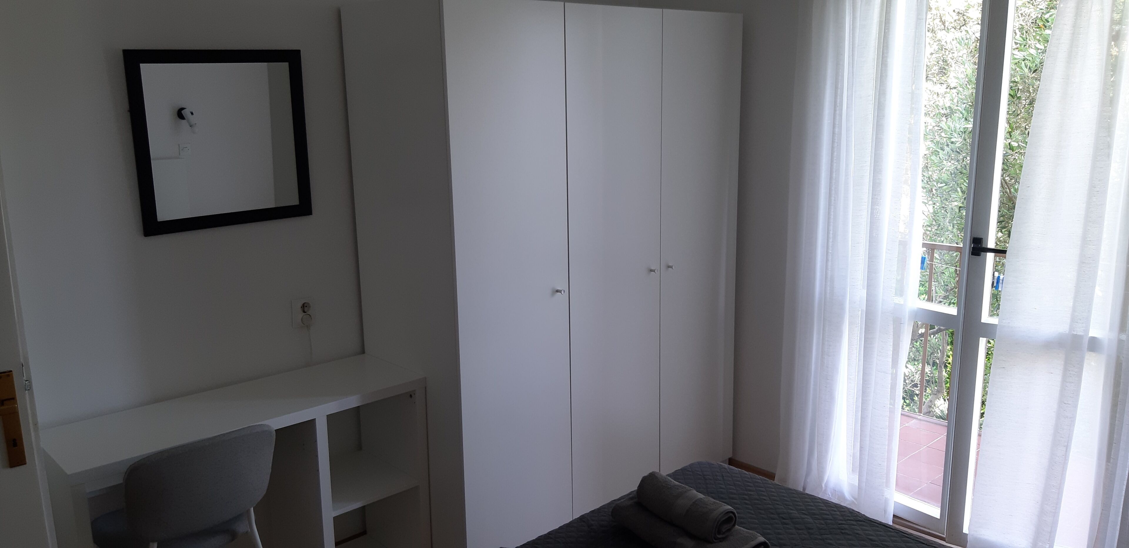 A room with a bed, a desk, a wardrobe, and a window with curtains.