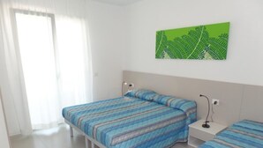 Camera da letto con due letti, un quadro con motivi a foglie verdi e una porta bianca.