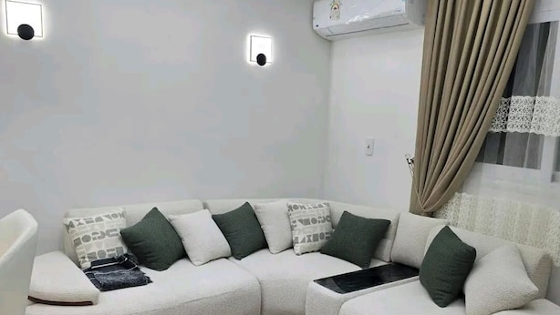 Een moderne woonkamer met een modulaire bank, een houten salontafel, inbouwspots en een airconditioner.