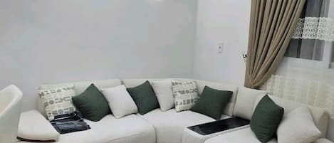 Una sala de estar moderna con un sofá seccional, una mesa de centro de madera, iluminación empotrada en el techo y un equipo de aire acondicionado.