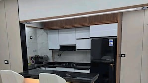 Een moderne keuken met twee witte barkrukken, een zwarte koelkast en houten keukenkastjes.