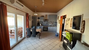 A compact kitchen with a dining area, a sliding glass door leading to an outdoor patio, and a small storage unit with a mirror. - Directly on the beach with sea view (Vir)
