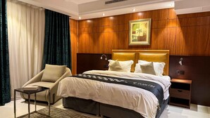 Quarto de hotel com cama, poltrona, mesa de cabeceira e parede de painéis de madeira.